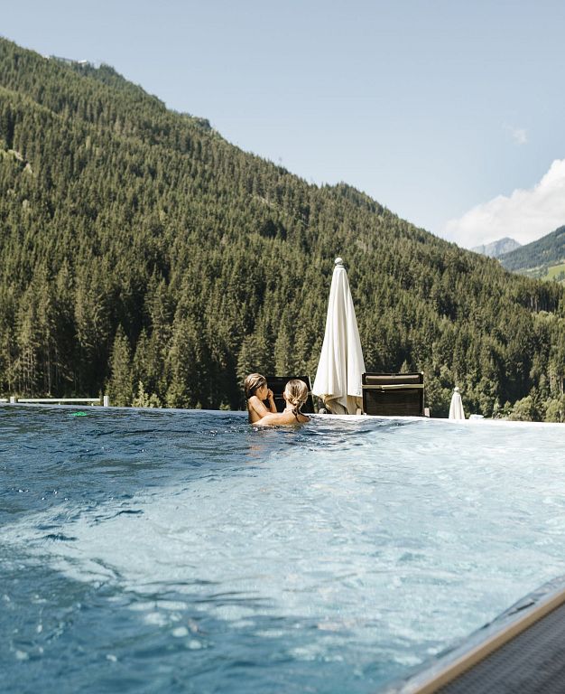 Mutter und Kind schwimmen im Infinity Pool beim Sommerurlaub mit Kindern in Österreich.