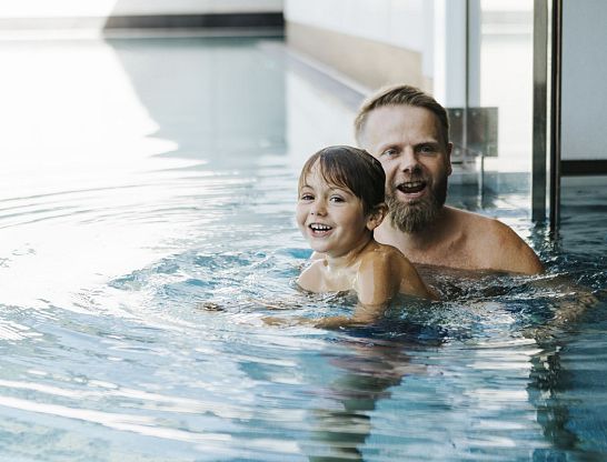 Vater und Kind schwimmen gemeinsam im Innenpool des Thurnerhof.