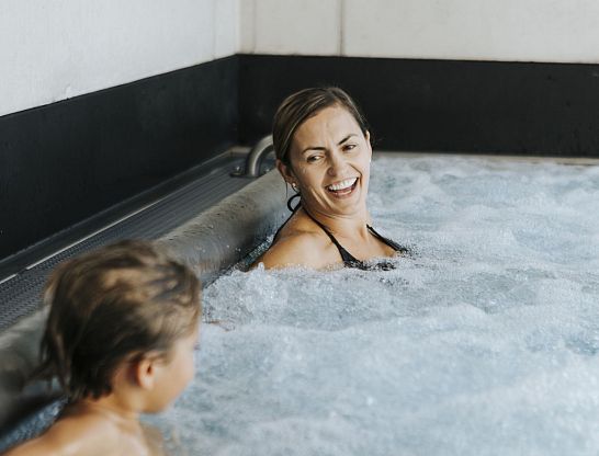 Mutter und Kind lachen im sprudelnden Wasser im Infinity Pool vom Hotel Thurnerhof Saalbach