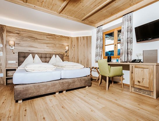 Doppelbett mit weißer Bettwäsche vor einer gemaserten Holzwand im Thurnerhof