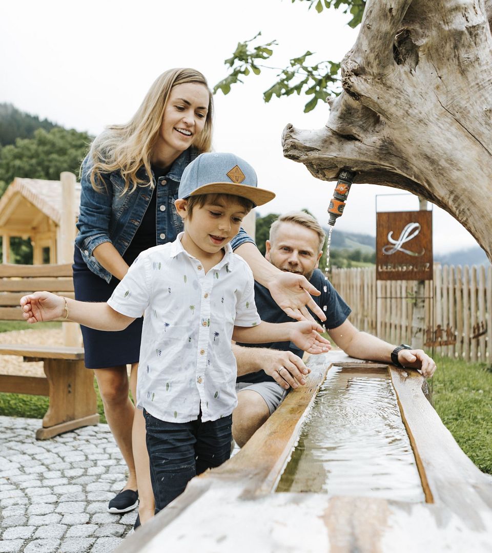 Familie spielt an einer Holz-Wasserbahn auf dem Spielplatz des Thurnerhof in Saalbach.