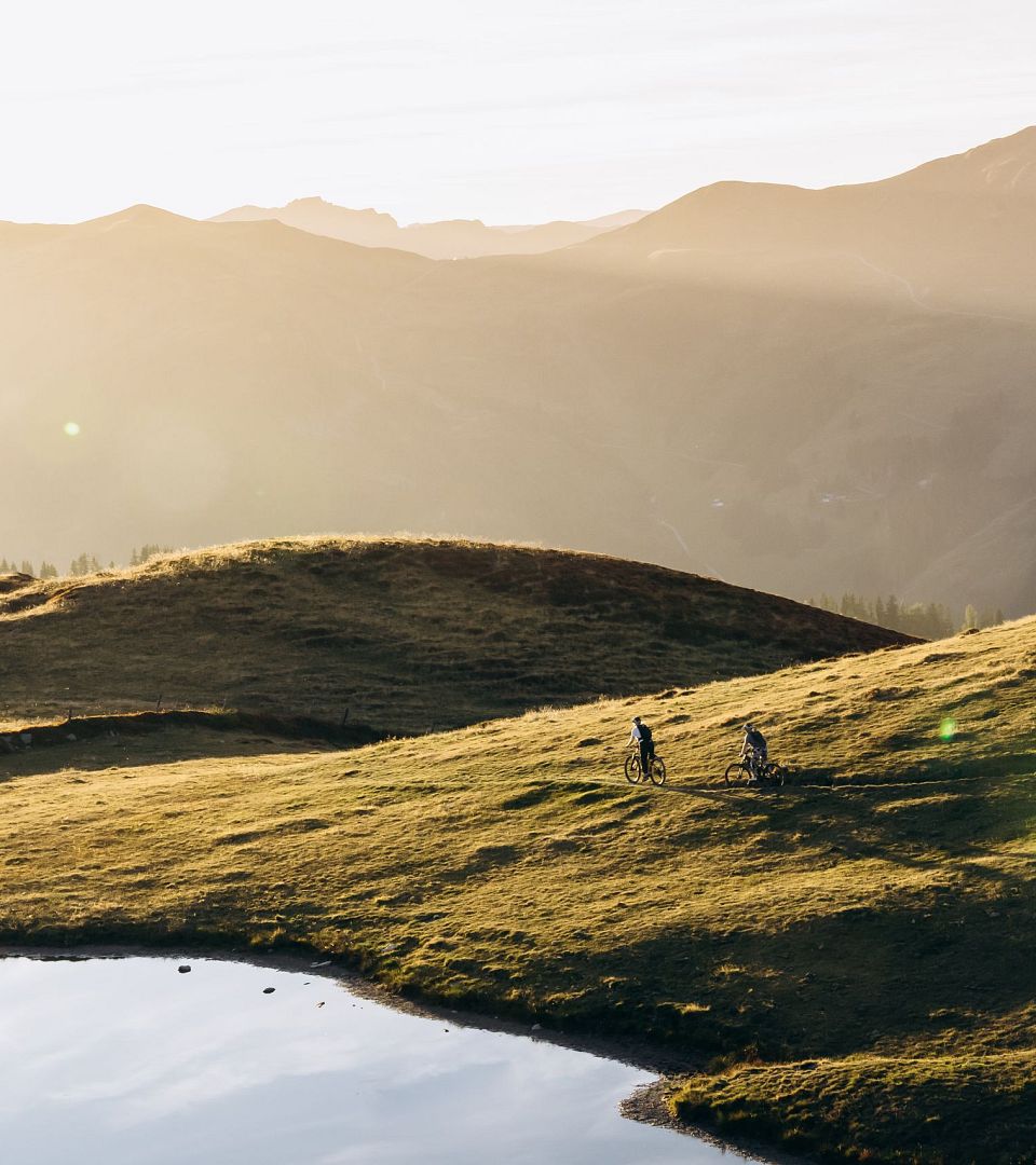 Mountainbiker fahren bei Sonnenuntergang über Almwiesen in Saalbach.