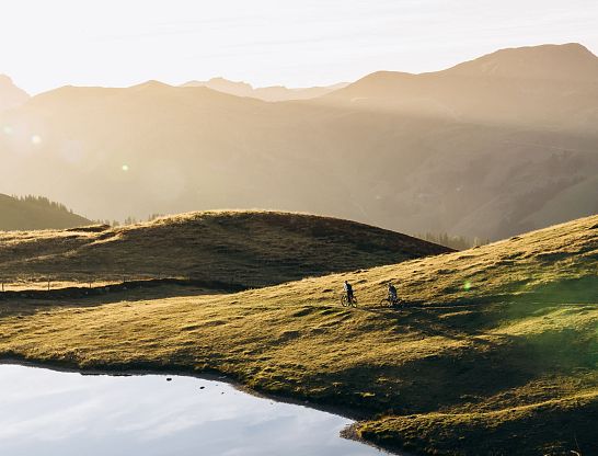 Mountainbiker fahren bei Sonnenuntergang über Almwiesen in Saalbach.