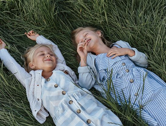 Zwei lachende Kinder liegen gemeinsam im hohen Gras beim Thurnerhof