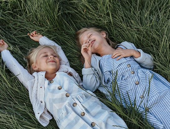 Zwei lachende Kinder liegen gemeinsam im hohen Gras beim Thurnerhof